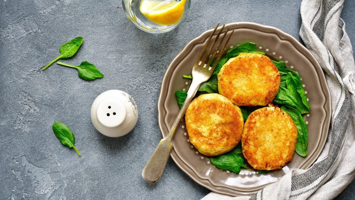 Drei Sellerie-Schnitzel auf einem Spinatbett auf einem Teller mit einer Gabel in der Draufsicht.