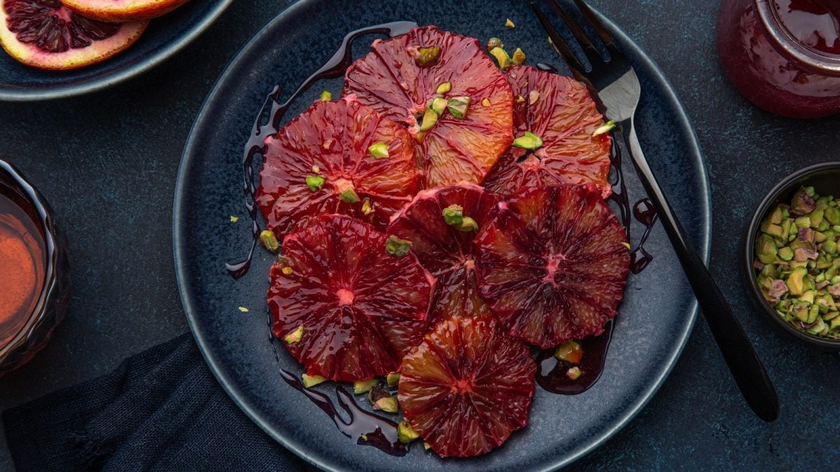 Ein schwarzer Teller mit Blutorangen-Carpaccio mit gerösteten Pistazien.