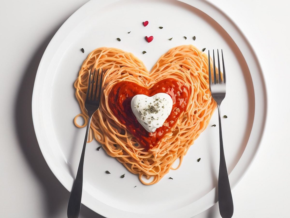 Ein Teller Spaghetti mit Marinara-Sauce, alles in Herzform drapiert, dazu zwei Gabeln, Draufsicht.