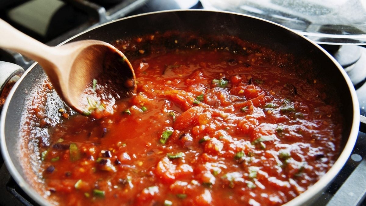 Spaghetti Pomodoro, köchelnd in einer großen, tiefen Pfanne, garniert mit frischem Basilikum und umgerührt mit einem Holzlöffel.
