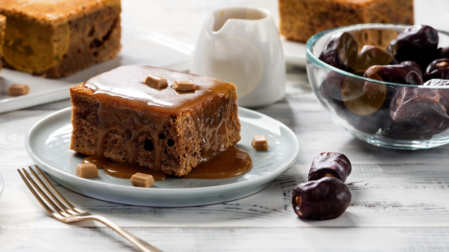 Toffee Pudding auf einem weißen Tisch mit einer Glasschale Datteln.