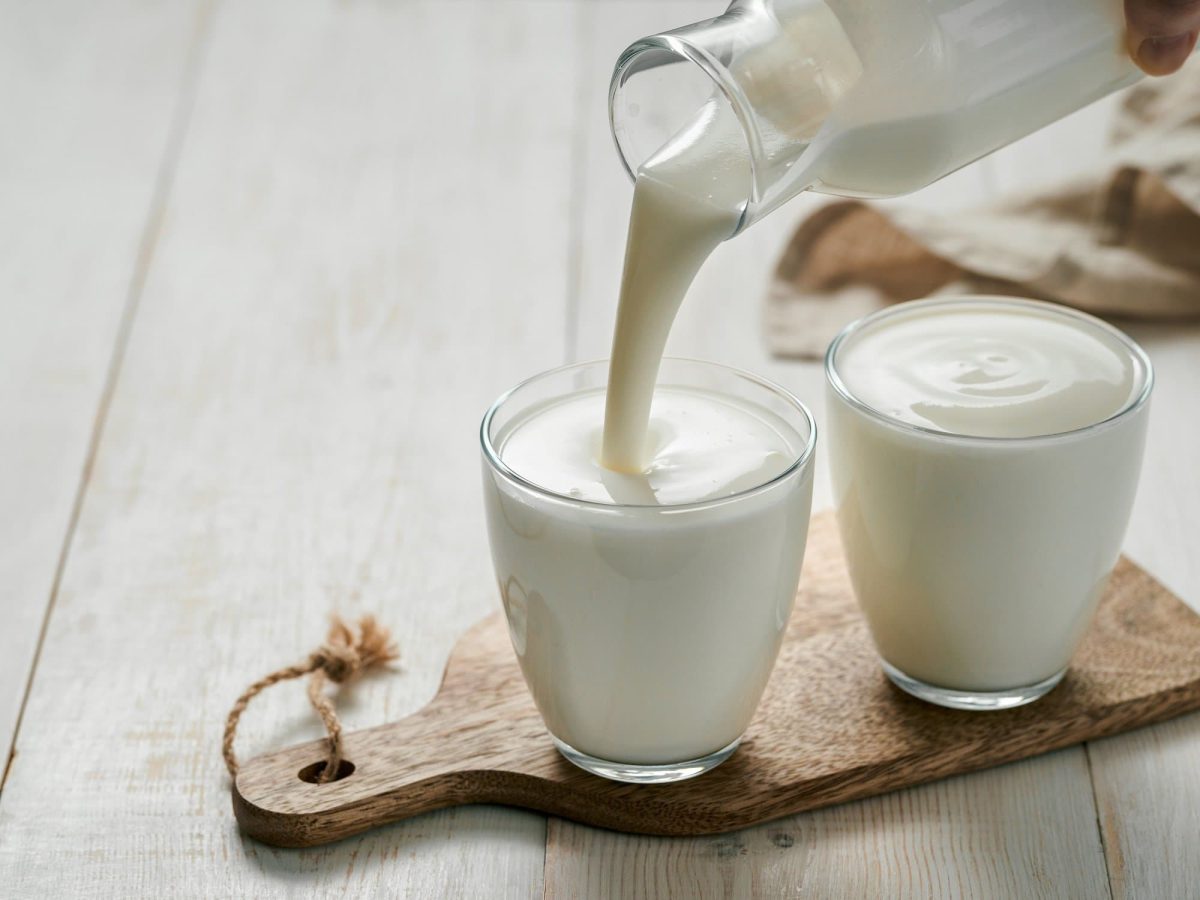 Zwei Gläser, in die selbst gemachte vegane Buttermilch gegossen wird, stehen auf einem Holzbrett.