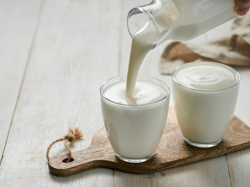 Zwei Gläser, in die selbst gemachte vegane Buttermilch gegossen wird, stehen auf einem Holzbrett.