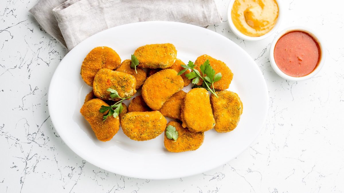 Ein TellerTofu Nuggets mit einem Schälchen eines weißen Dips, bestreut mit Petersilie, daneben zwei Dip-Schalen.