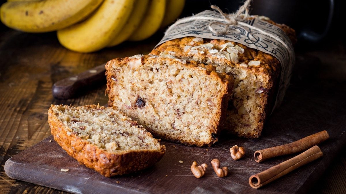 Ein angeschnittenes veganes Zimtbrot, daneben liegen Zimtstangen.