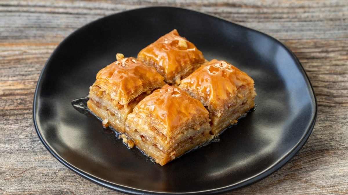 Vier Stücke Walnuss-Baklava auf einem schwarzen Teller auf Holzhintergrund.
