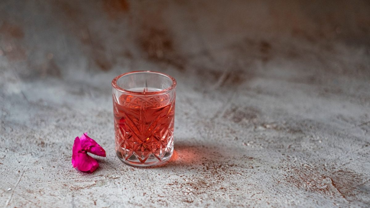Woo-Woo-Cocktail Woo Woo mit einer Blüte auf grauem Untergrund. Frontalansicht.