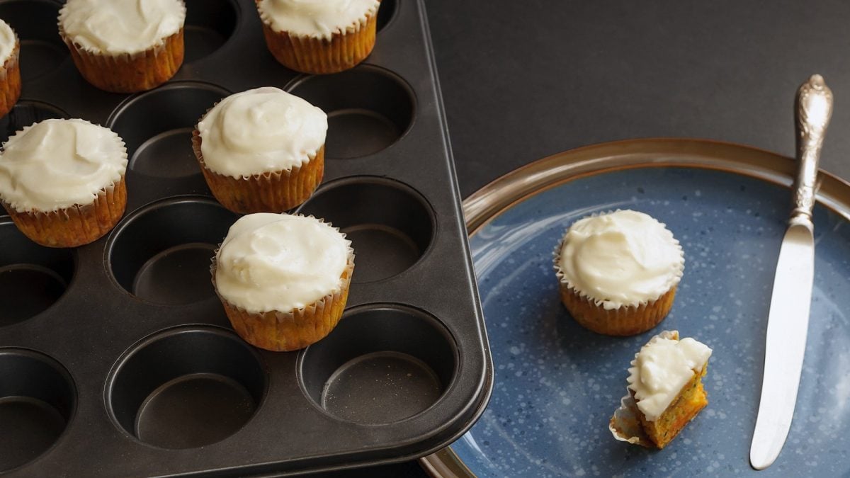 Ein Muffinblech mit Zimtschnecken-Muffins mit Frosting, daneben ein Teller, auf dem weitere Muffins liegen.