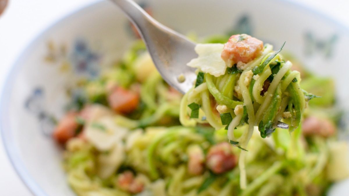 Ein weiß-blauer Teller mit der Zucchini-Carbonara und eine rGAbel mit aufgerollter Zucchini und der Sauce.