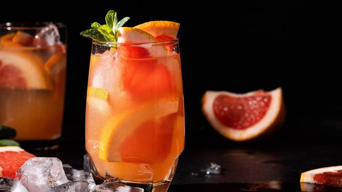Zwei Gläser mit dem Aperol Paloma auf einem dunklen Tisch mit schwarzem Hintergrund.