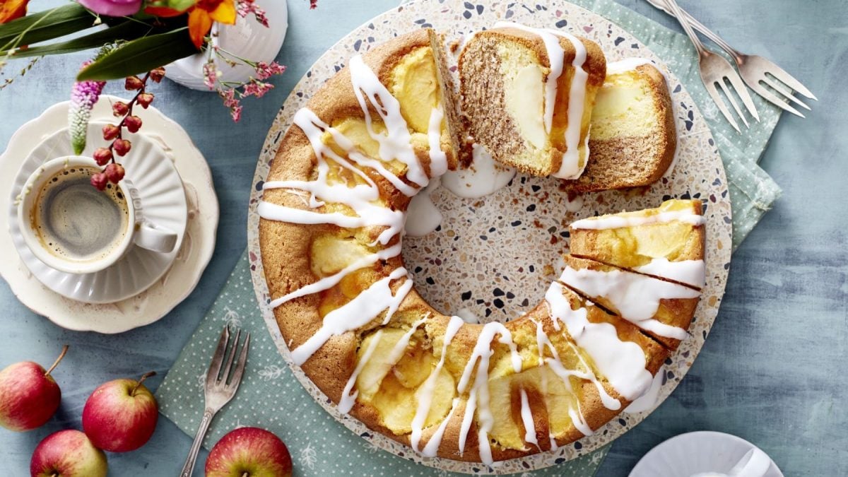 Auf einem Teller liegt Apfel-Kranzkuchen. Er ist mit Zuckerguss überzogen und mit Äpfeln gefüllt.