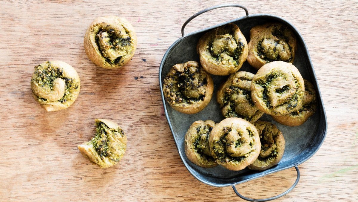 Bärlauch Pizza-Rolls in blauer Form auf Holz. Daneben weitere. Draufsicht.