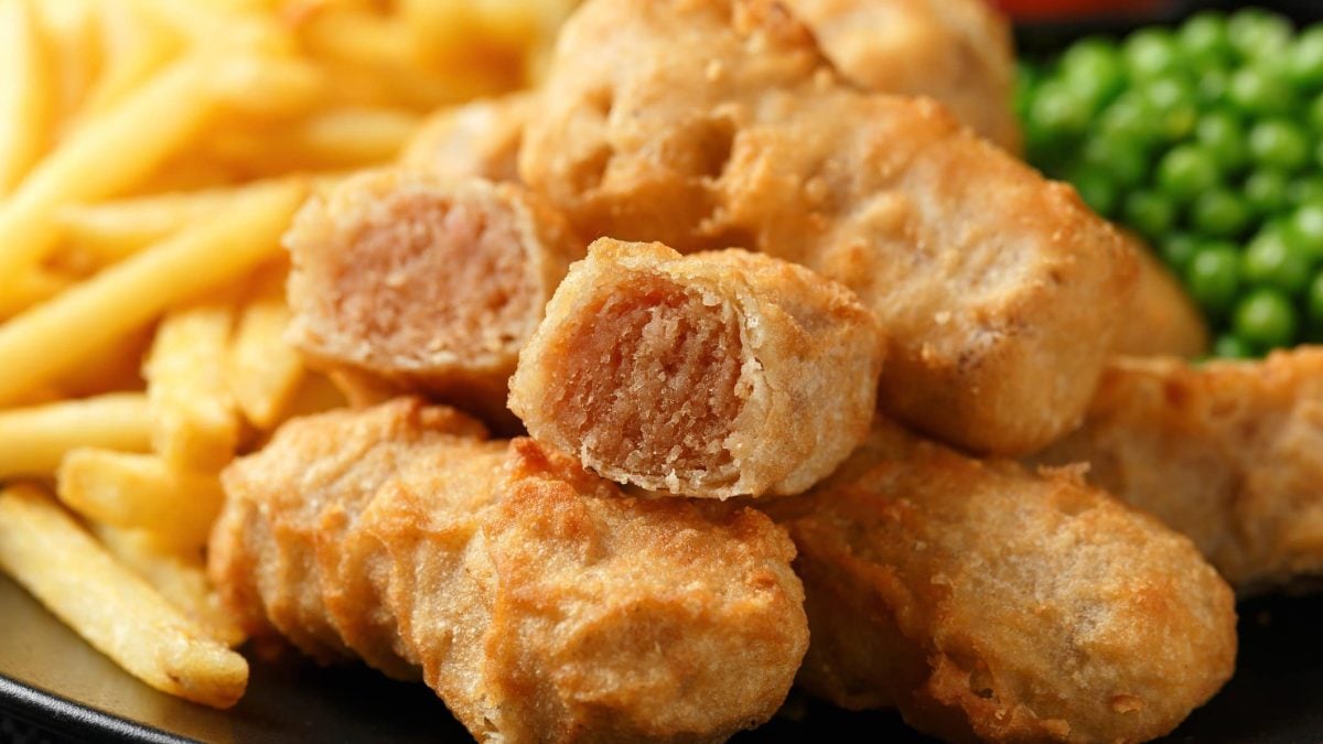 Irische Beer-Battered Sausages mit Pommes und Erbsen auf Teller. Frontalansicht.