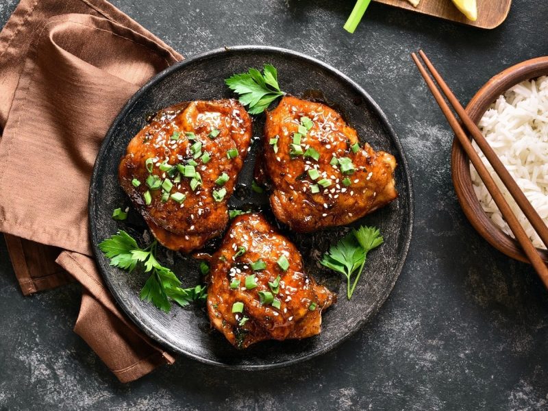 Einen schwarzen Teller mit Caramel Coco Chicken auf einem grauen Steintisch.