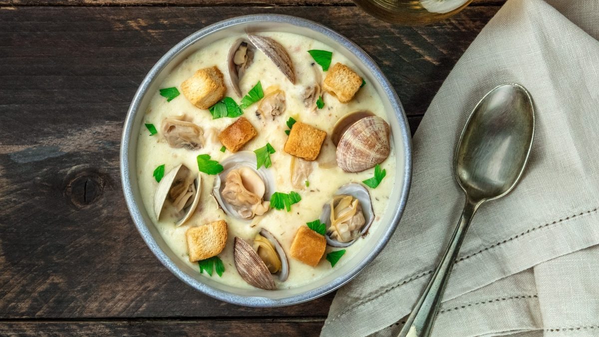 Eine graue Schale mit der Muschelsuppe auf einem dunklen Holztisch.