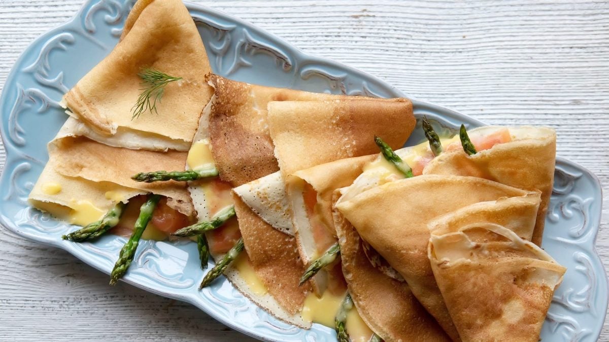Einige Crepes mit Lachs und Spargel gefüllt und zu Viertel gefalten auf einem blauen länglichen Teller von oben fotografiert.