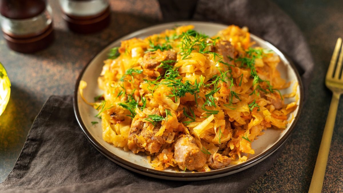 Ein weißer Teller mit schwarzem Rand, darauf der Curry-Kohl. Alles auf dunklem Untergrund mit einer goldenen Gabel.