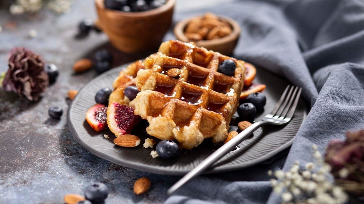 Draufsicht: Haferkleie-Waffeln mit Beeren und Mandeln liegen auf einem dunklen Teller auf einem dunklen Untergrund.