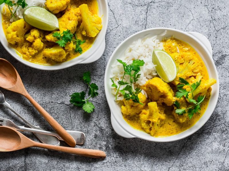 Zwei tiefe Teller mit Bananen-Curry mit Blumenkohl auf einem grauen Tisch.