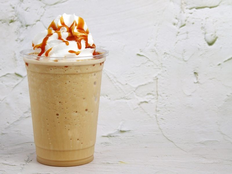 Ein Becher mit Biscoff Milkshake vor einem grauen Hintergrund.