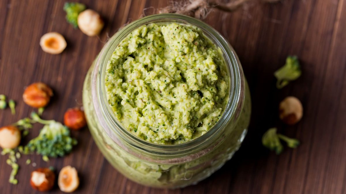 Ein Glas mit Brokkoli-Pesto auf einem braunem Holztisch.