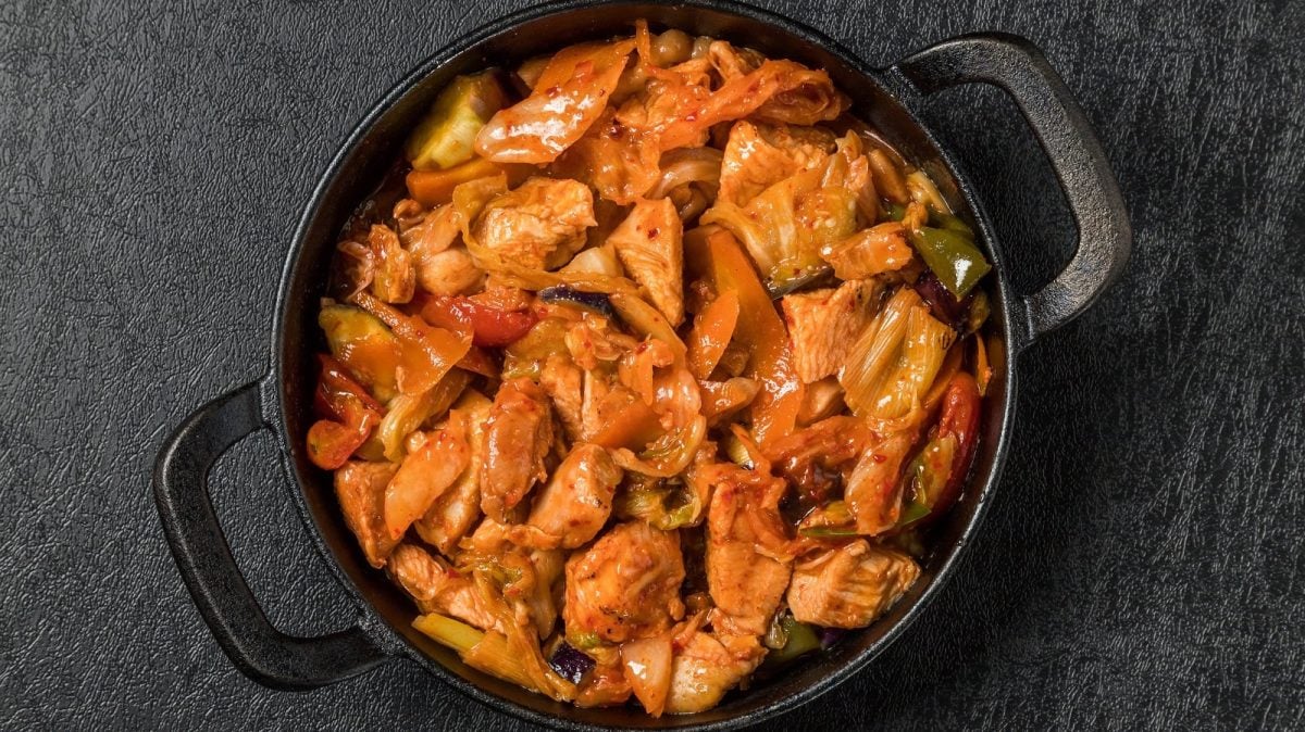 Ein schwarzer Topf mit Dak Galbi auf einem schwarzen Tisch.
