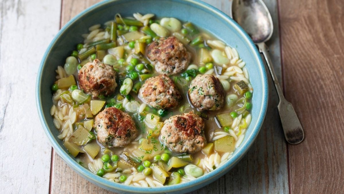 Ein tiefer blauer Teller mit grüner Minestrone auf einem Holztisch.