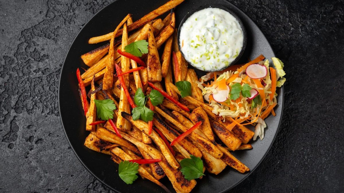 Ein schwarzer Teller mit Harissa-Pastinaken mit Knoblauch-Dip.