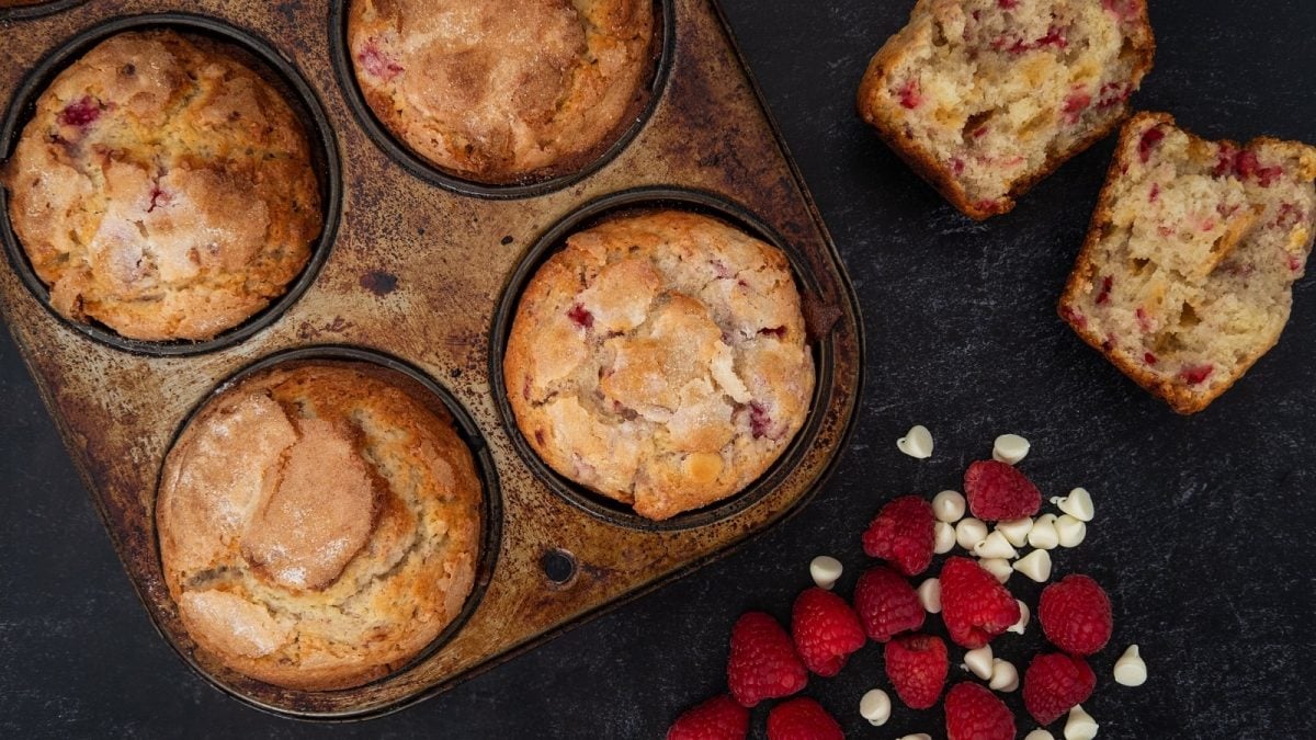 Ein Blech mit Himbeer-Muffins mit weißer Schokolade auf dunklem Hintergrund.