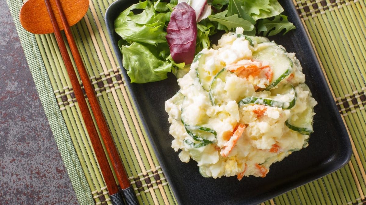 Ein schwarzes Tablett mit japanischer Kartoffelsalat auf einer Bambusmatte.
