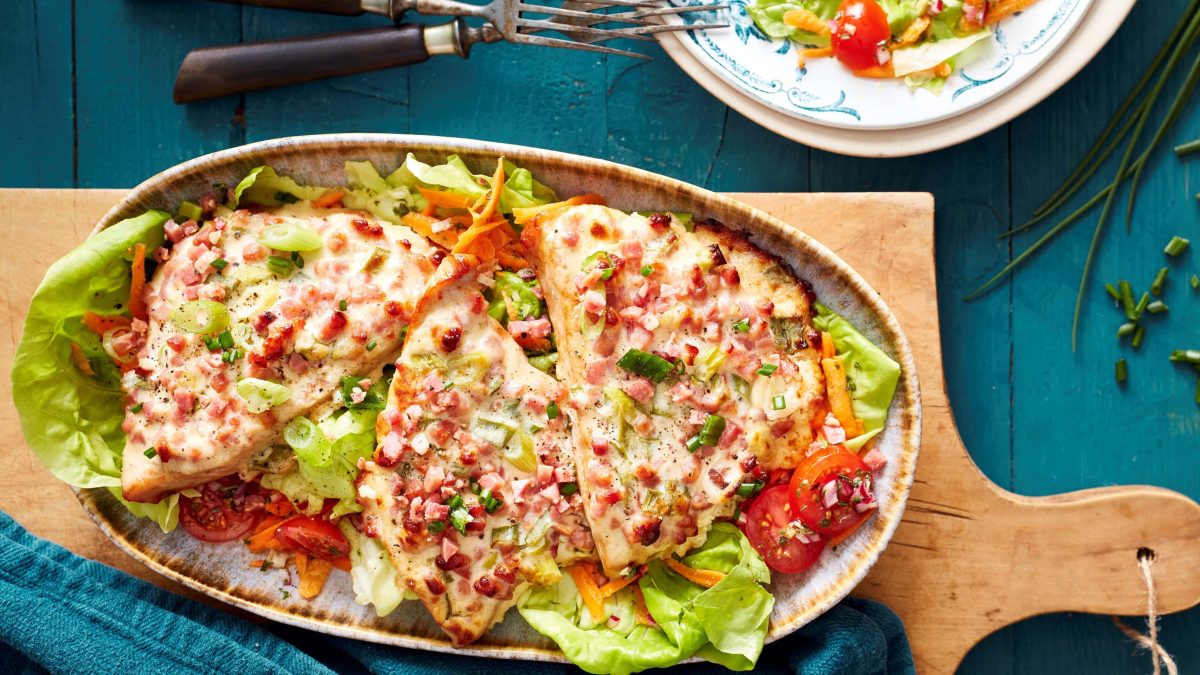 Flammkuchen-Schnitzel auf Salatbett in der Draufsicht.