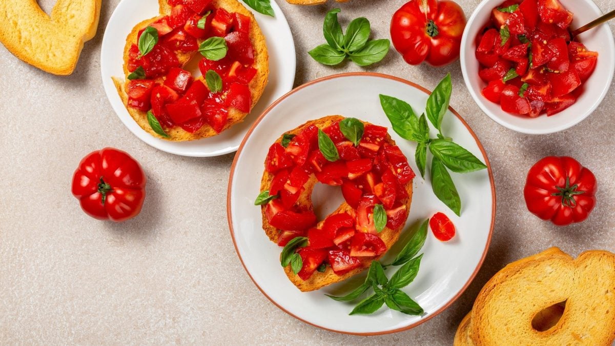 Draufsicht: Italienische Friselle mit frischen Tomaten und Basilikum liegen auf einem hellen Untergrund.