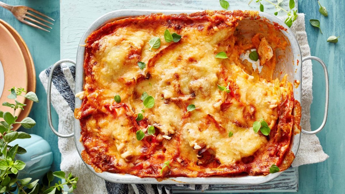 Hähnchen-Lasagne mit Paprika in der Draufsicht auf einem Küchentuch vor hellblauem Untergrund.