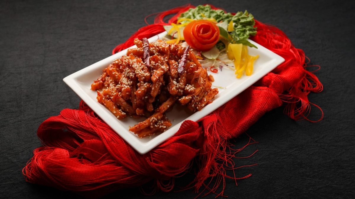 Honig-Chili-Süßkartoffelpommes mit Sesam mit Beilagen auf weißem Teller auf rotem Tuch. Draufsicht.