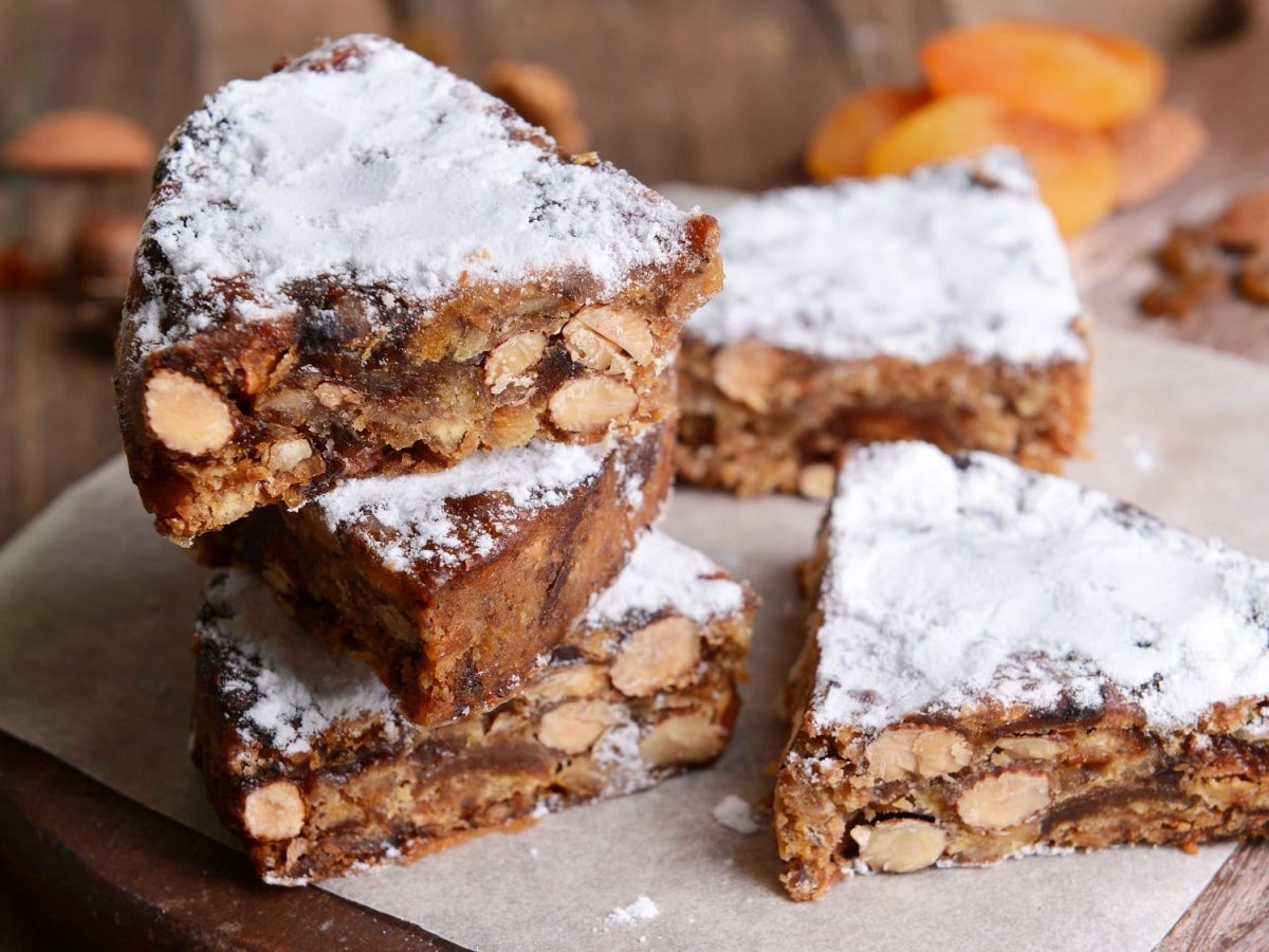 Frontalsicht: mehere Stücke Panforte liegen gestapelt auf einem Holztisch. es handelt sich um einen italienischen Kuchen.