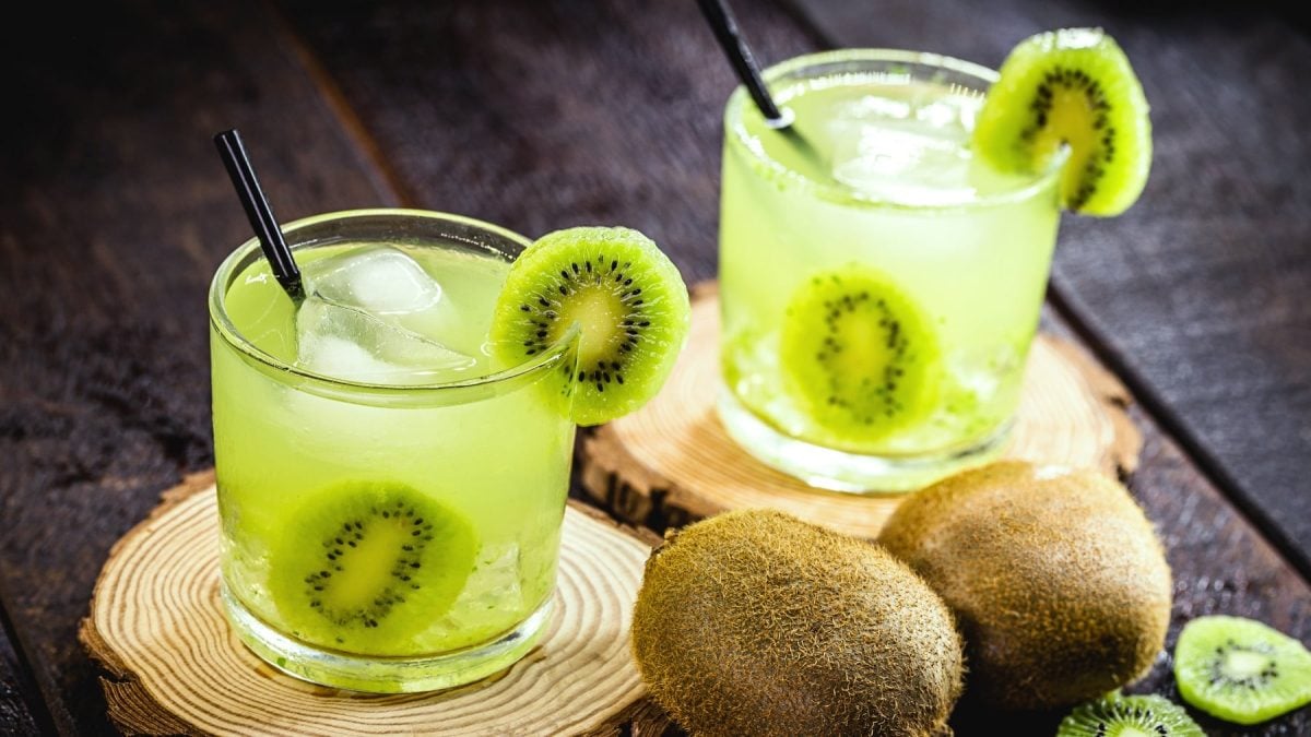 Zwei grüne Cocktails mit Kiwi auf zwei Holzscheiben und dunklem Untergrund.
