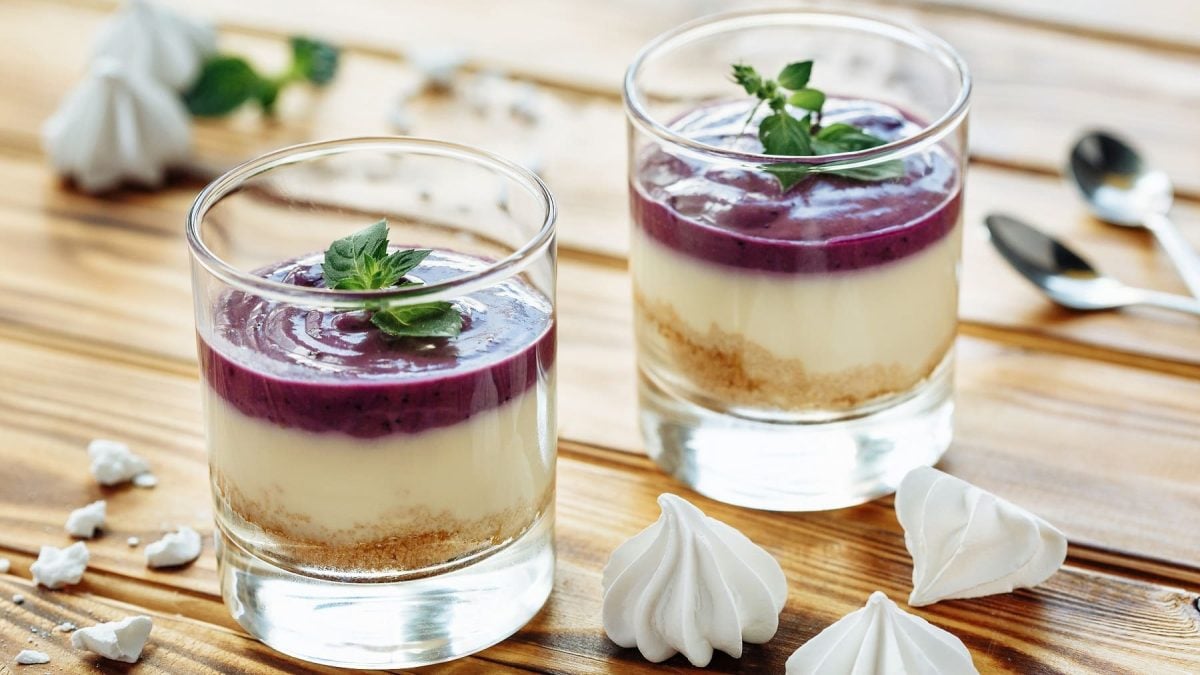 Zwei Gläser mit der Mandel-Panna-Cotta auf einem Holztisch mit zwei silbernen Löffeln.