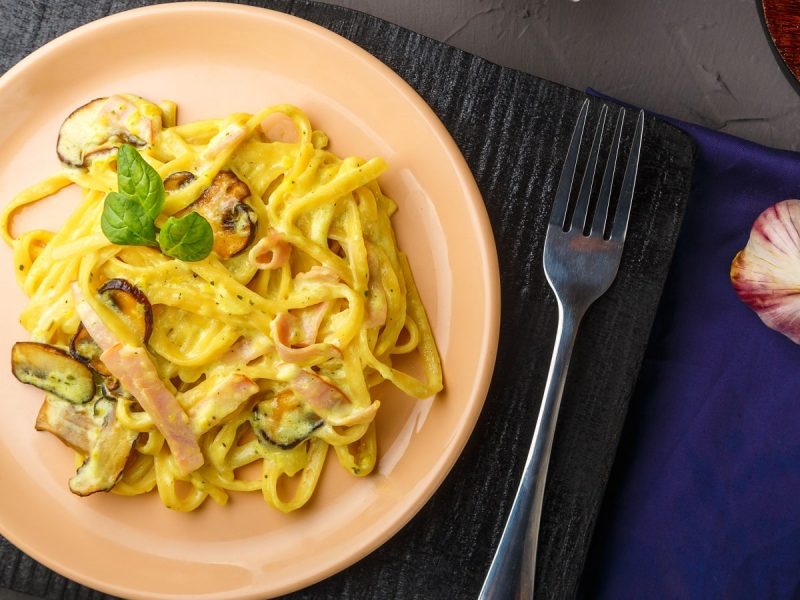Ein runder rosafarbener Teller mit Miso Carbonara auf einem schwarzen Holzbrett.