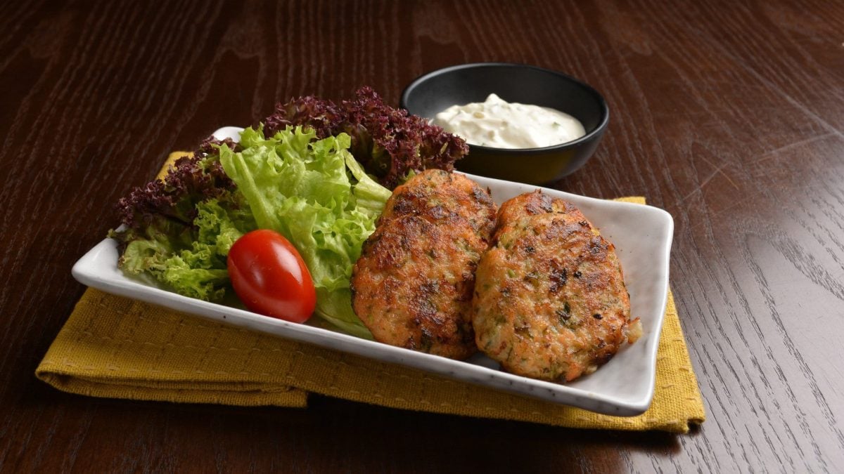 Mshat Zahrah knuspige Blumenkohl-Taler aus Palästina auf weißem Teller mit Salat auf Holzbrett. Oben eine Schale mit Dip. Frontalansicht.