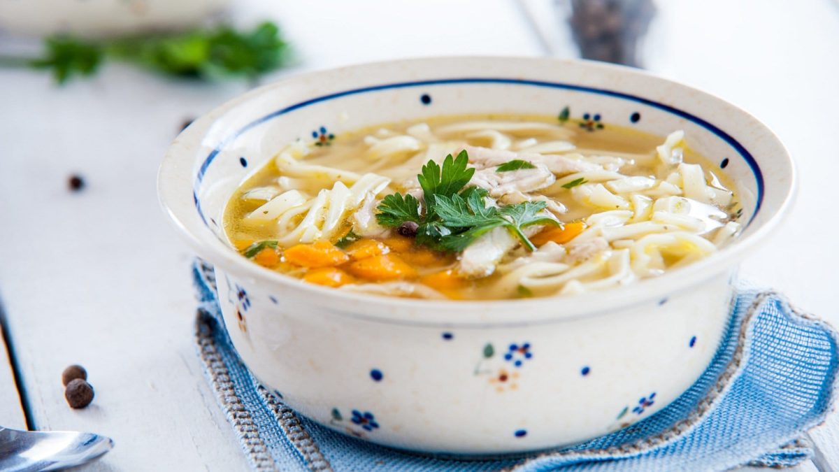 Eine gemusterte Schüssel Nudelsuppe mit Gemüse und Petersilie.