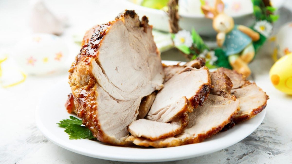 Osterbraten mit Honigglasur auf weißem Teller und hellem Untergrund. Im Hintergrund Deko. Frontalansicht.