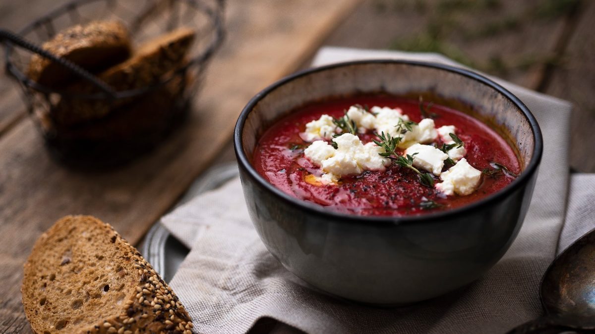 Eine schwarze Schale mit der Rote Bete Suppe und Ziegenkäse auf einem dunklen Holztisch mit ein paar Scheiben dunklem Brot.