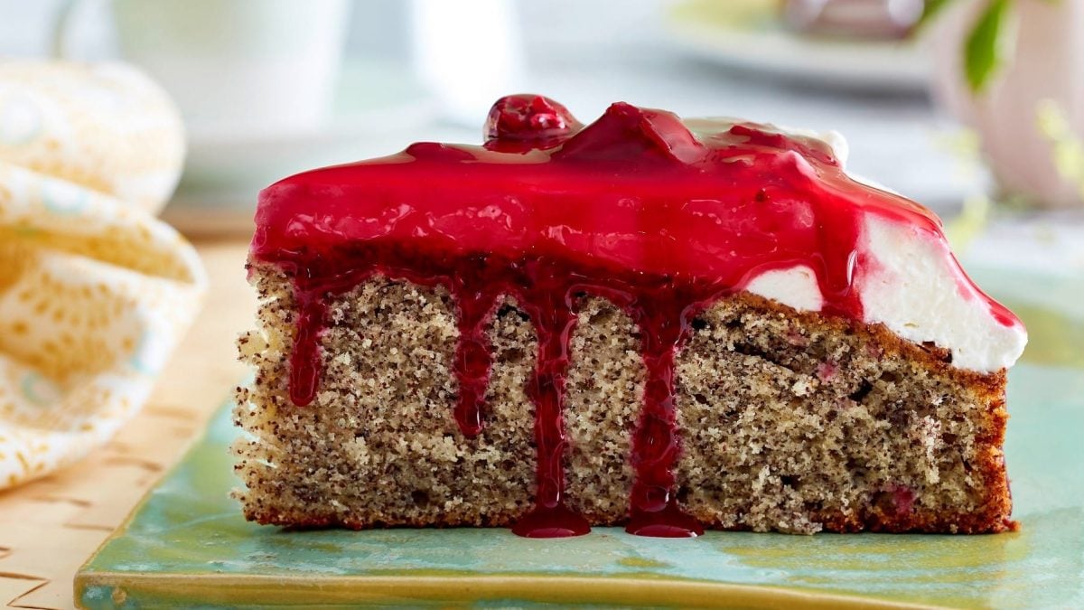 Ein Stück Rote-Grütze-Mohnkuchen von der Seite auf grünem Untergrund.