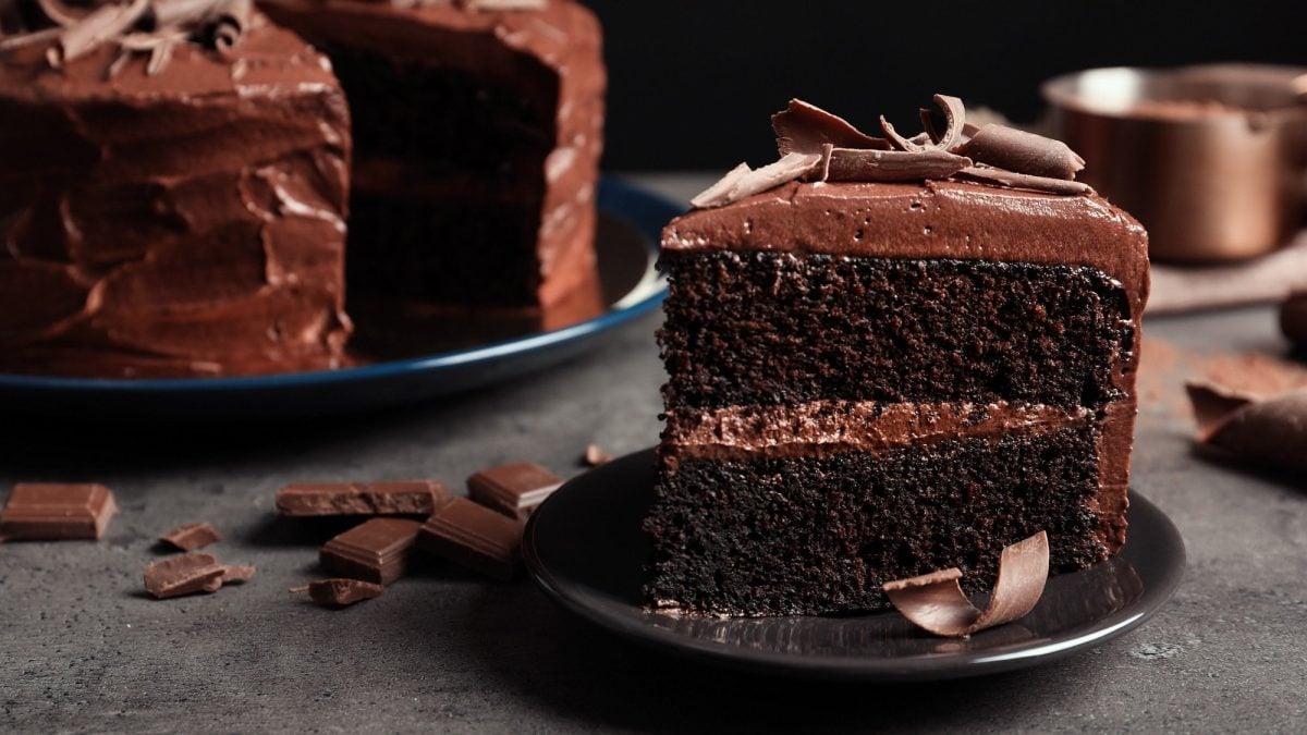 Ein Stück vegane Schokoladentorte auf einem Teller, im Hintergrund die angeschnittene Torte.