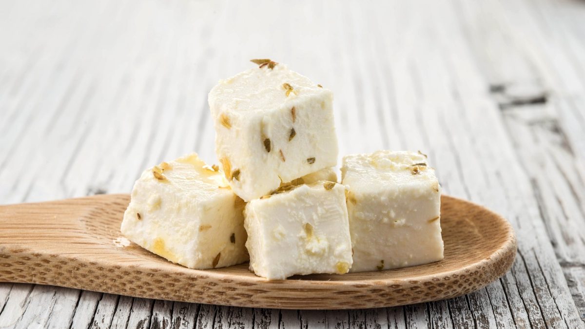 Vegane Feta-Würfel mit Kräutern auf einem Holzlöffel.