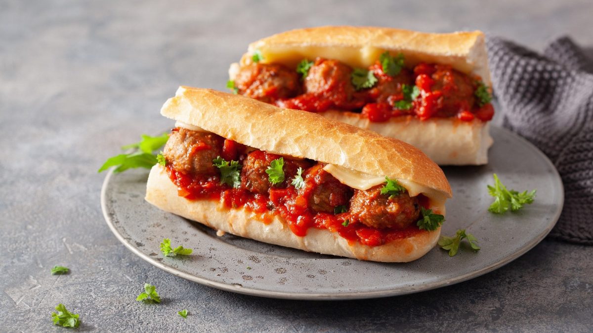 Zwei vegane Meatball Subs mit Tomatensauce, veganem Käse und Petersilie auf einem Teller.
