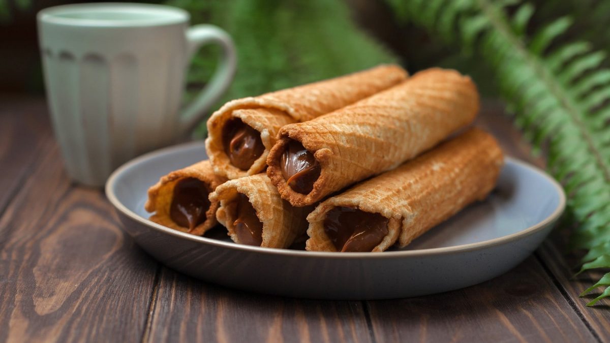 Fünf Waffelrollen mit Dulce de Leche auf einem Holztisch.