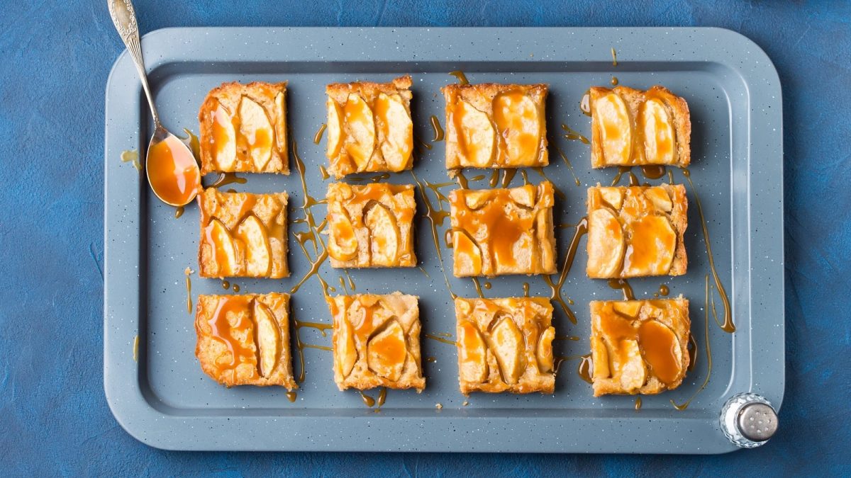Ein blaues Backblech mit Apfel-Zimt-Blondies auf einem blauen Tisch.