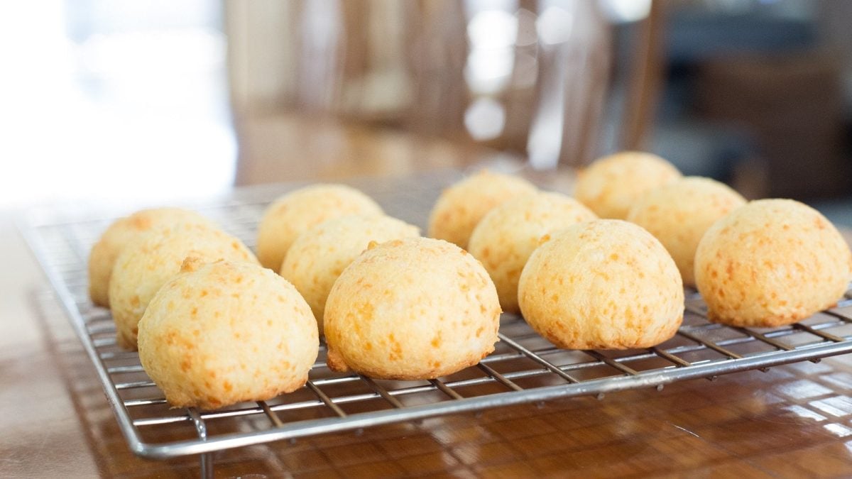 Frontalsicht: auf einem Untergrund aus Holz steht ein Gitter auf dem runde Parmesan-Brötchen abkühlen.
