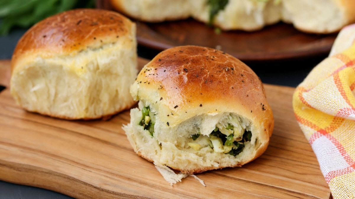 Gefüllte Bärlauch-Brioche mit Ei auf Holzbrett auf Holztisch. Frontalansicht.